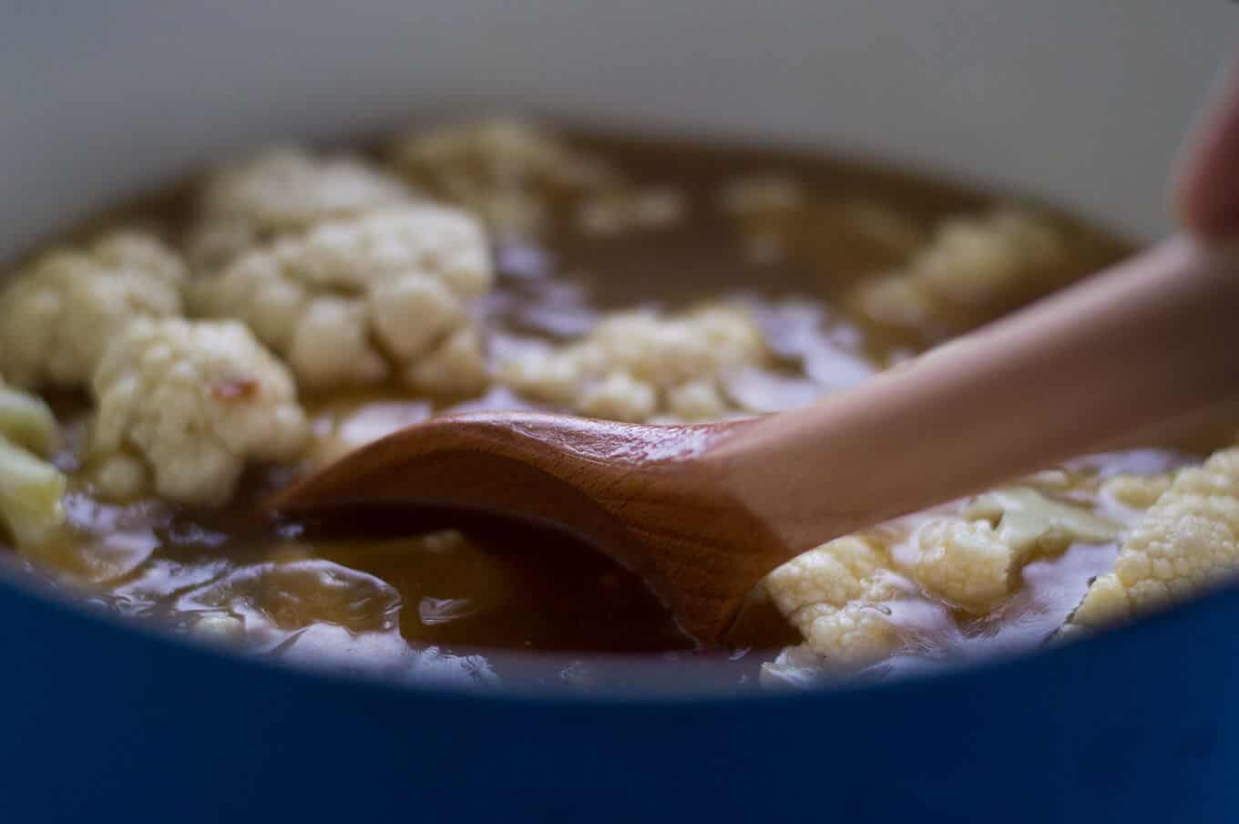 A wooden spoon stirring soup in a saucepan.