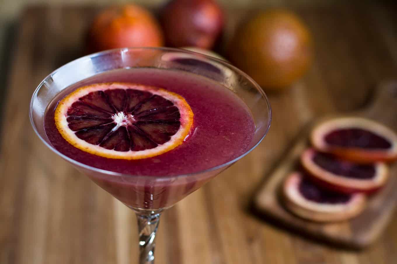 Close up of a blood orange ginger martini garnished with a slice of blood orange.