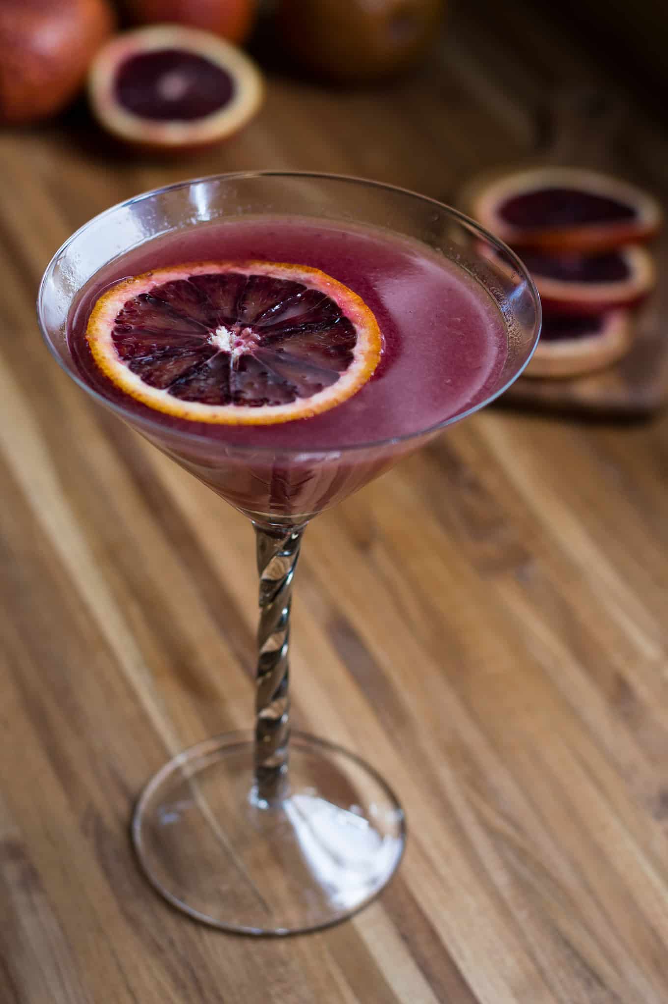 A blood orange ginger martini in a martini glass topped with sliced blood orange.