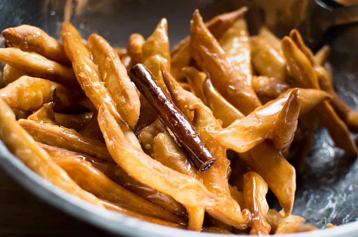 Cooked Trinidadian kurma and a cinnamon stick in a stainless steel bowl coated in warm syrup.