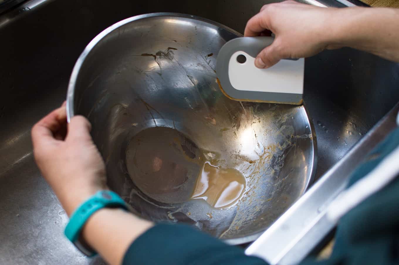 A person\'s hands holding and washing a dirty bowl with a dish squeegee.