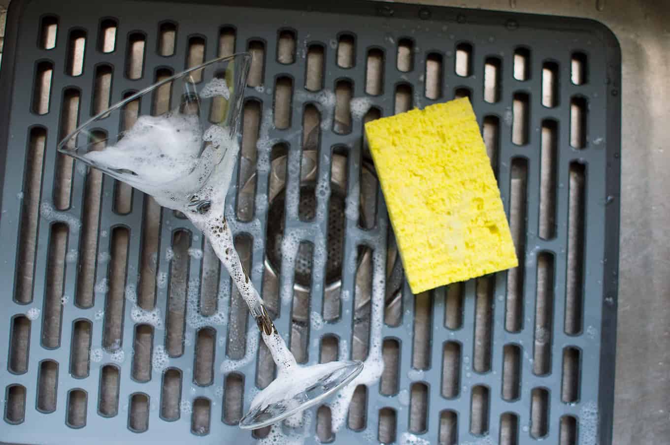 A soapy martini glass and sponge resting in a kitchen sink.