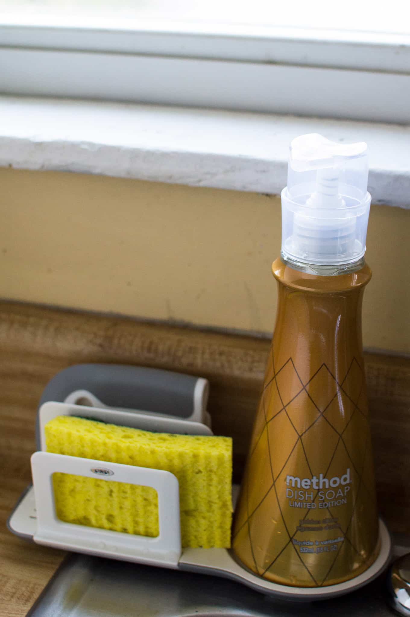 A bottle of dish soap, sponge, and dish squeegee on a sink organizer.