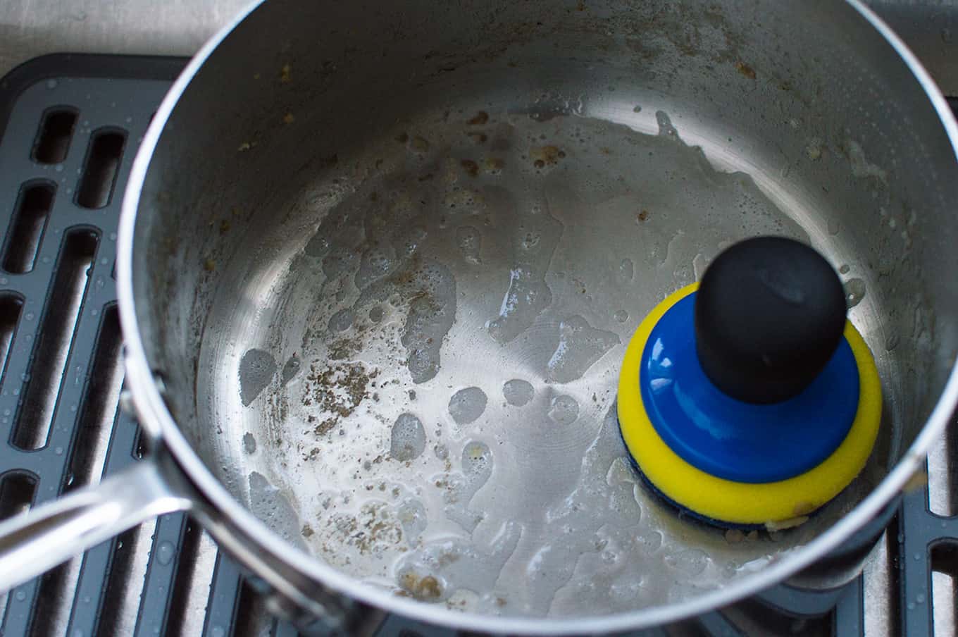 Close up of a soapy saucepan with a palm brush inside.
