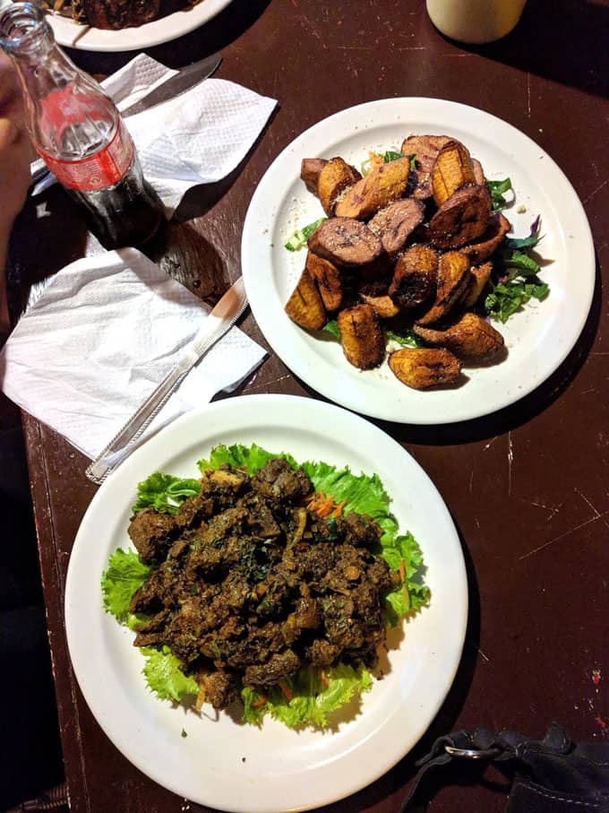 A plate of geera pork and plate of fried plantains on a table.