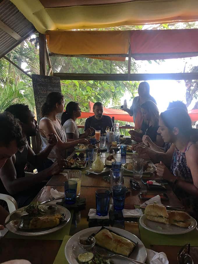 A group of people sitting at a table with food at Shore Things in Trinidad and Tobago.