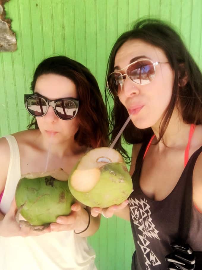 Two women drinking coconut water out of fresh coconuts.