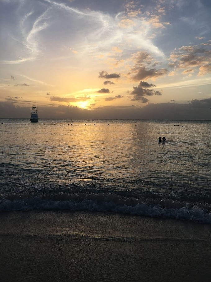 A sunset overlooking a beach with two people and a boat in the water at a distance.