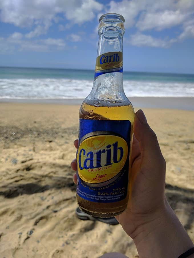 A hand holding a bottle of beer at the beach.