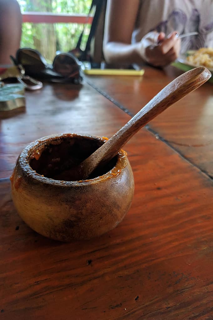 A wooden bowl of hot sauce with a wooden spoon inside.