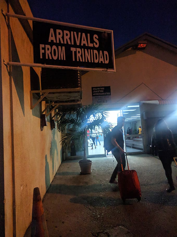 A sign at the airport that reads \"arrivals from trinidad.\"