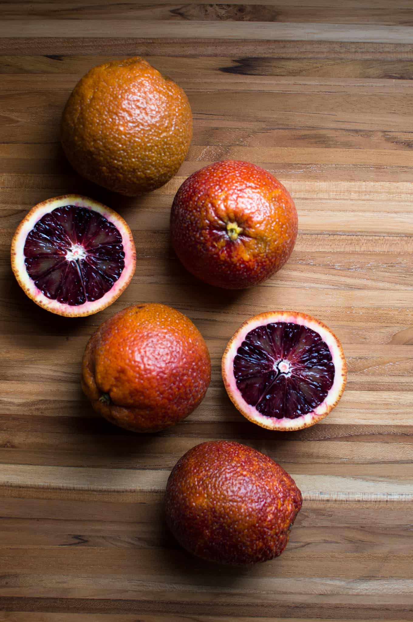 Assorted whole and cut blood orange on a wooden cutting board.