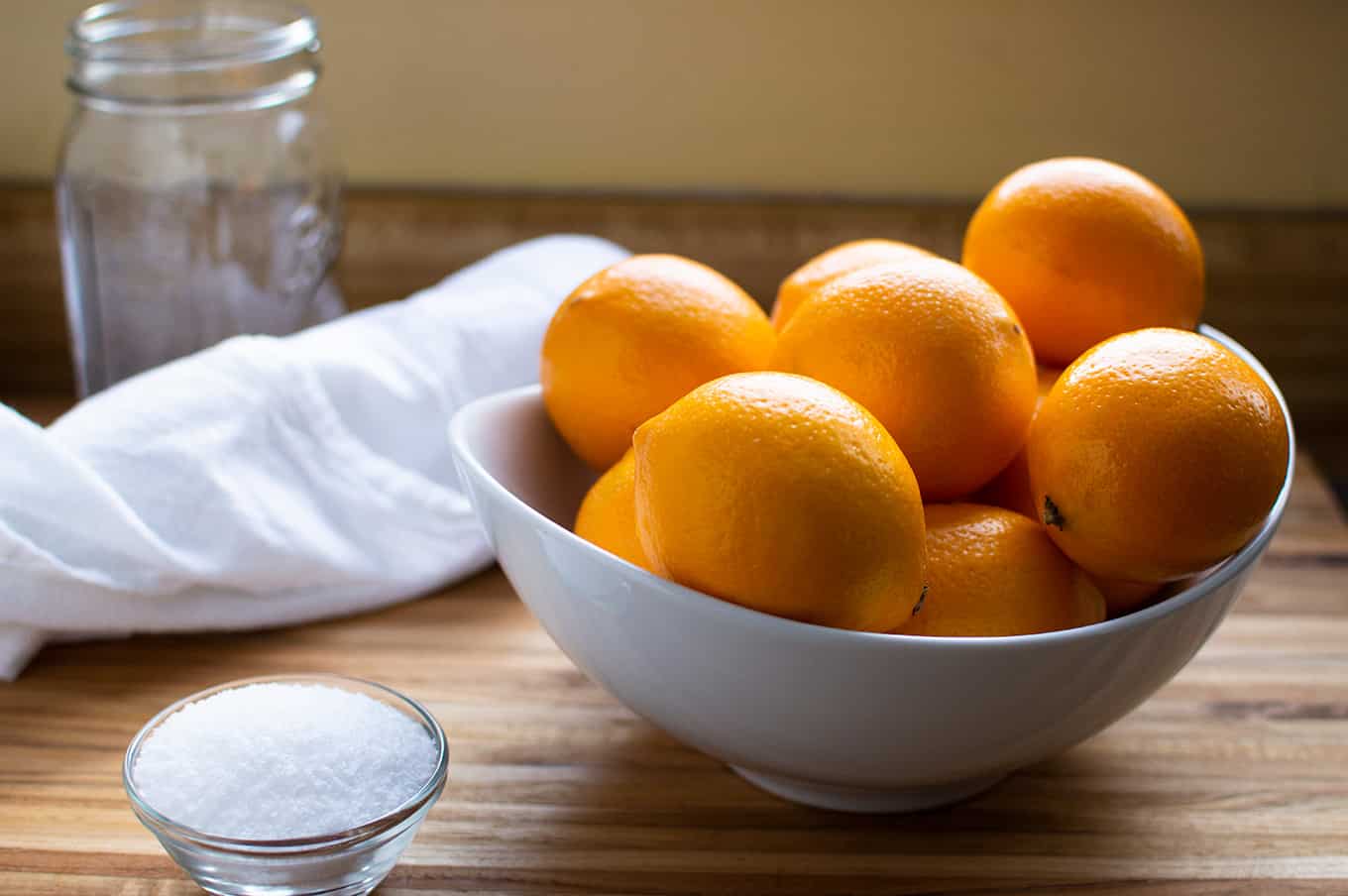 A large bowl of lemons, small bowl of salt, and an empty jar on a countertop.