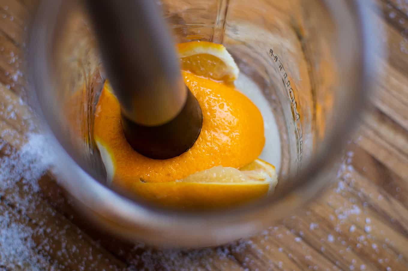 Close up of a muddler pressing down on a cut lemon in a mason jar.