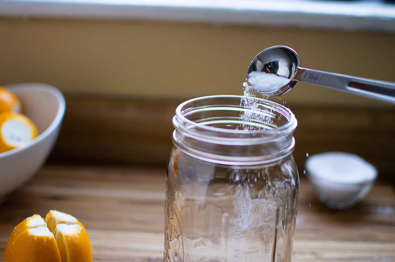 A measuring spoon pouring salt into a mason jar.