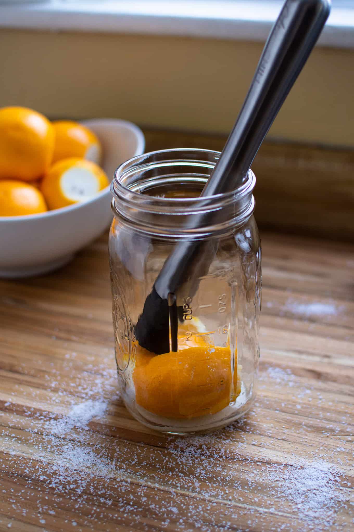 A mason jar with a cut lemon and muddler inside.