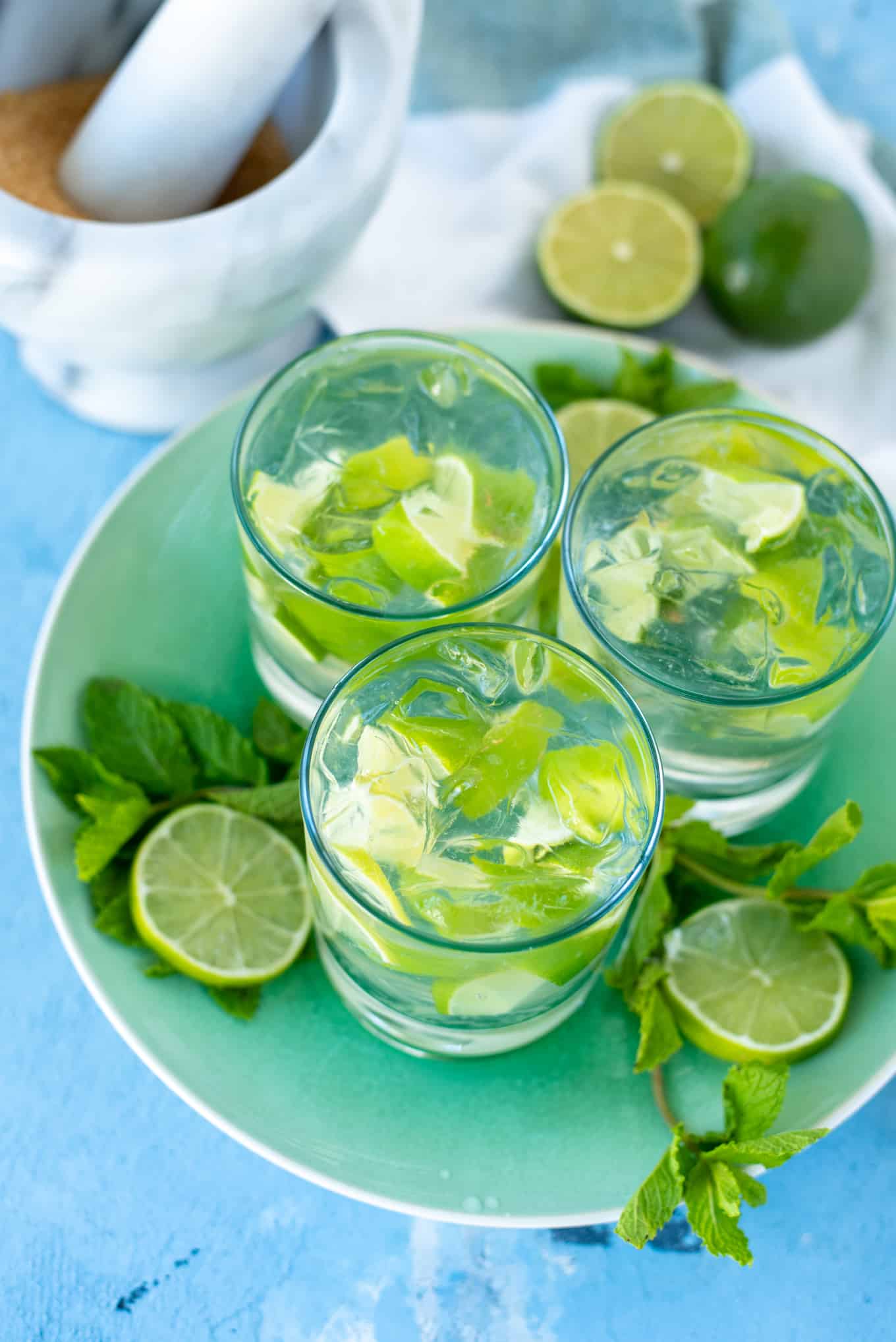 Three glasses of caipiroska on a tray decorated with sliced lime and fresh mint.