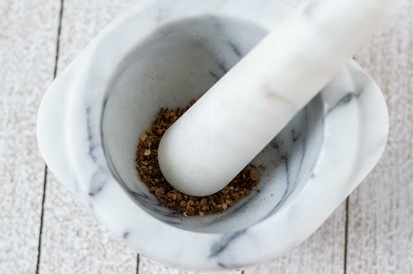 Whole spices being ground in a mortar and pestle.