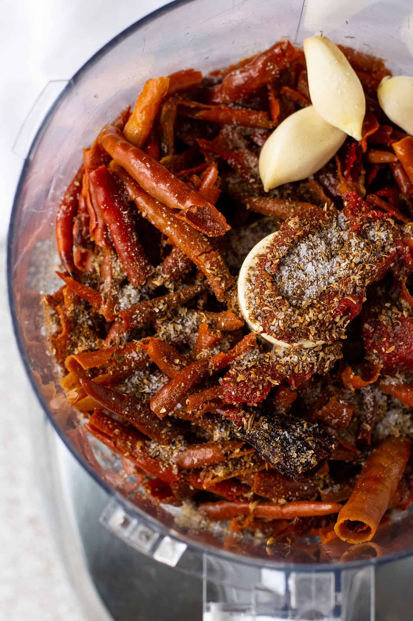 Close up of chiles, garlic cloves, and spices in a food processor.