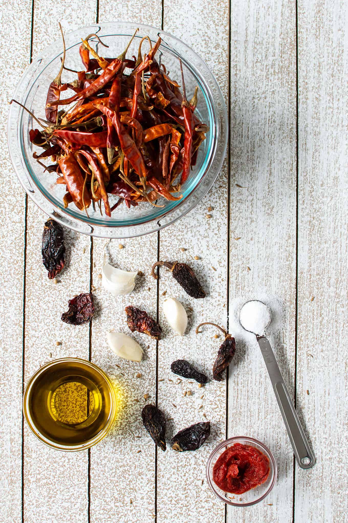 Dried chiles, garlic cloves, salt, and olive oil on a table.