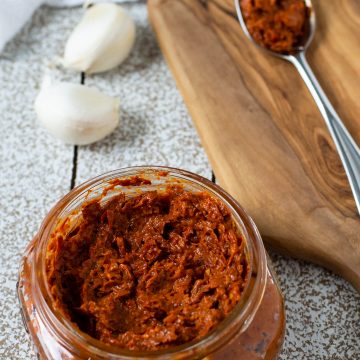 A small jar of harissa paste with a spoon of harissa paste on a table.