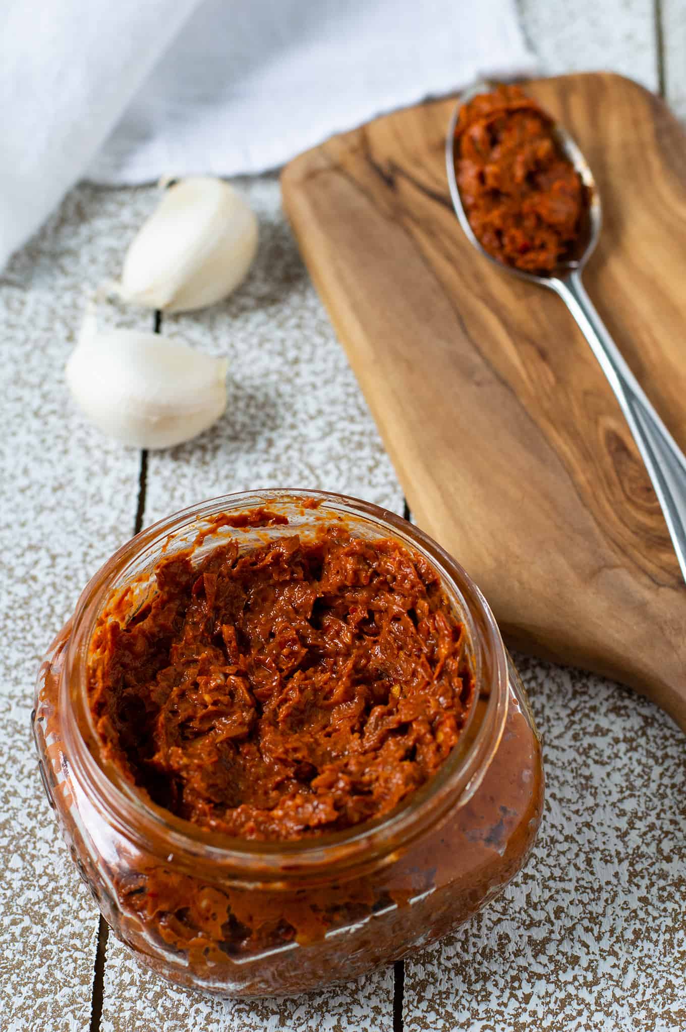 A small jar of harissa paste with a spoon of harissa paste on a table.