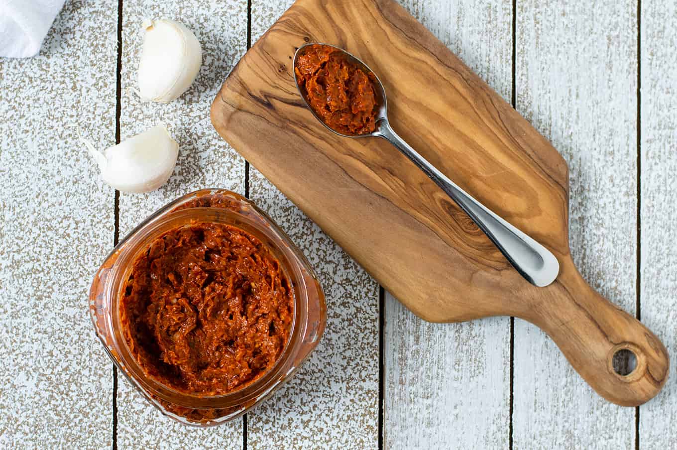 Top-down view of harissa paste in a small jar and a spoon of harissa paste on a table.