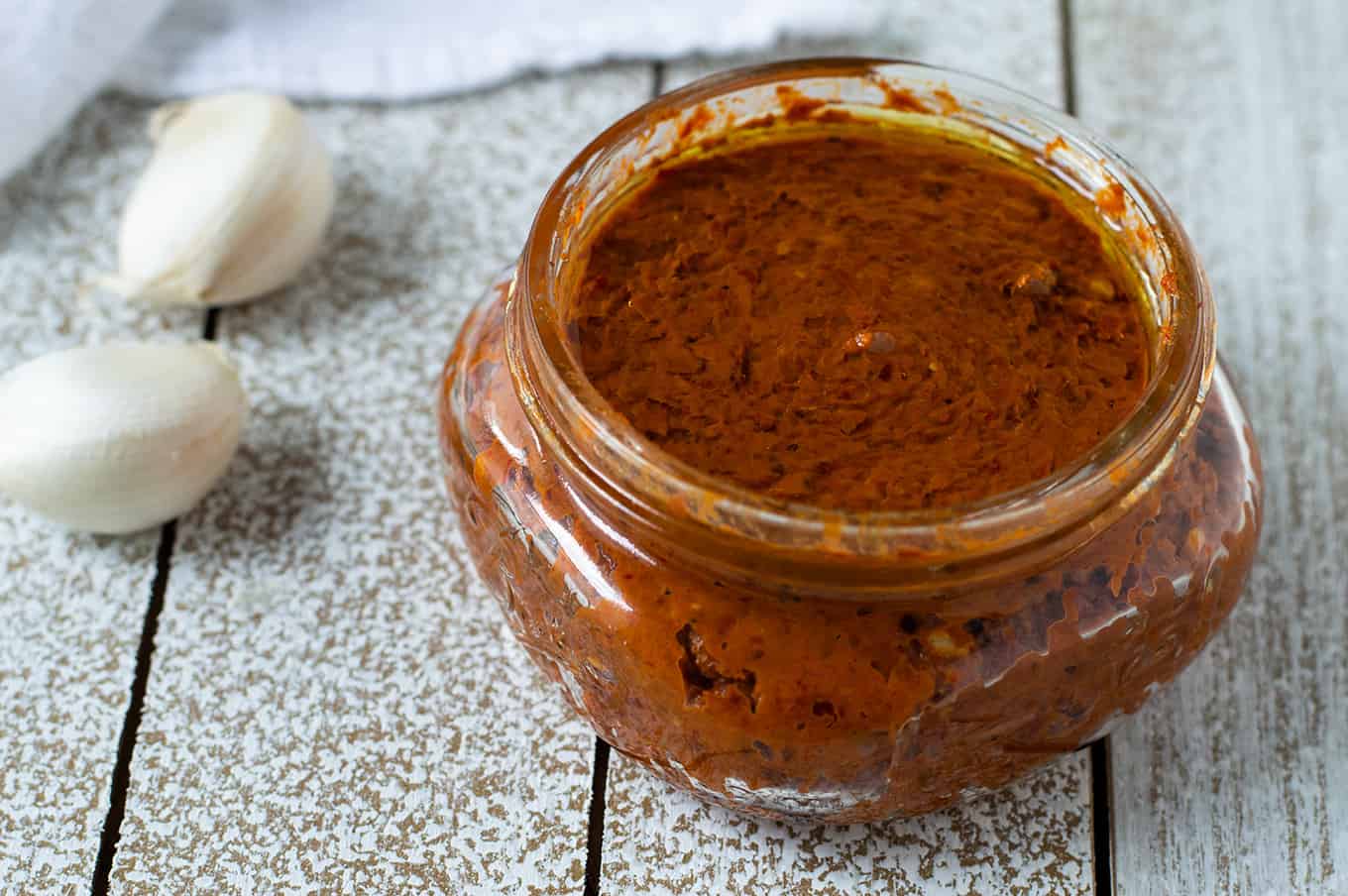 Harissa paste in a small glass jar topped with olive oil.