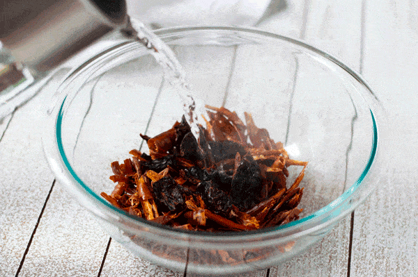 A gif of hot water being poured into a bowl of dried chiles.