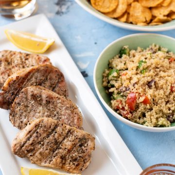 A plate of pork chops and bowl of quinoa salad on a table.