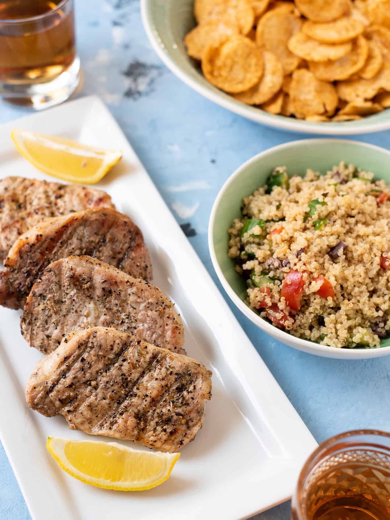A plate of pork chops and bowl of quinoa salad on a table.