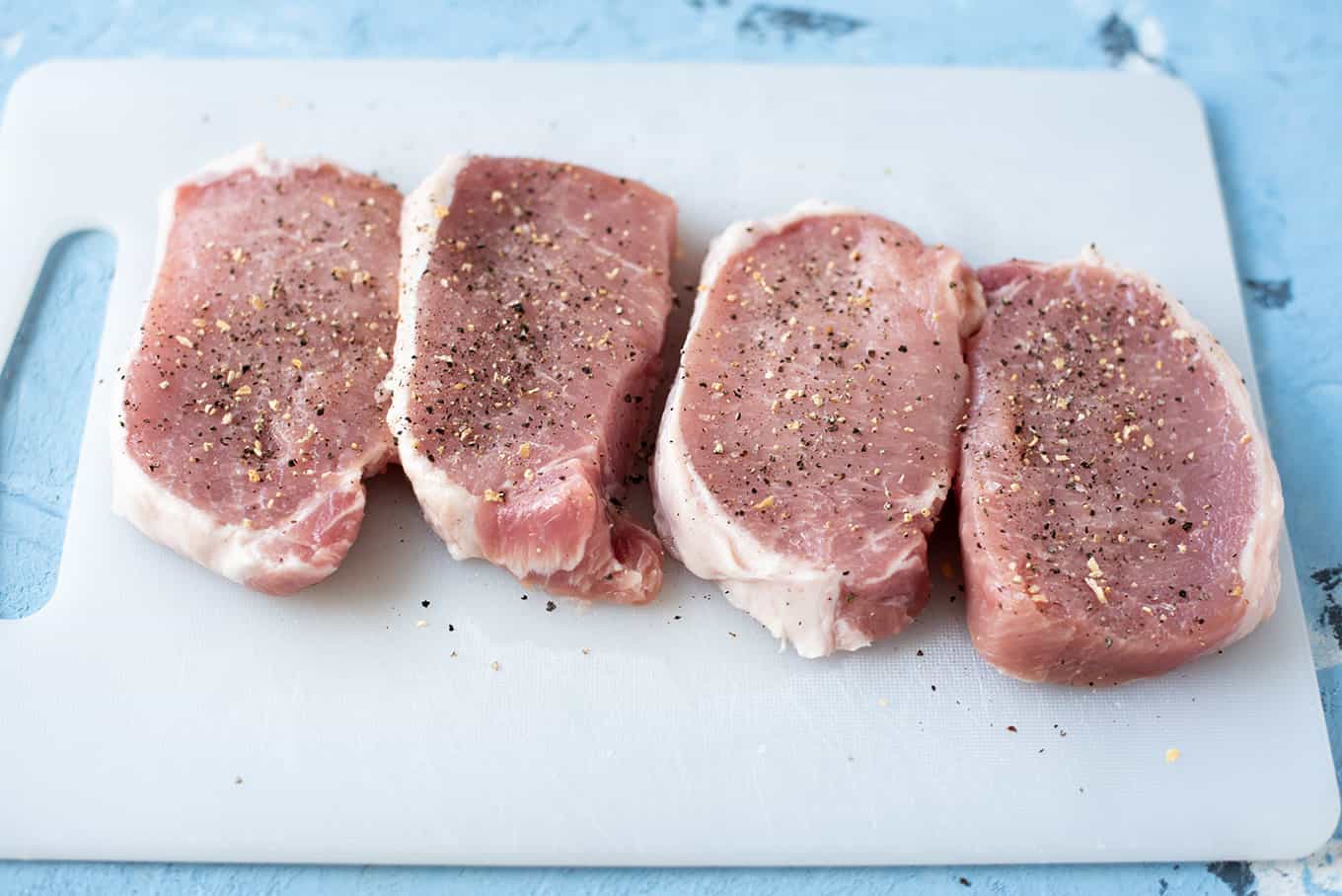 Sliced and seasoned raw pork chops on a cutting board ready for grilling.