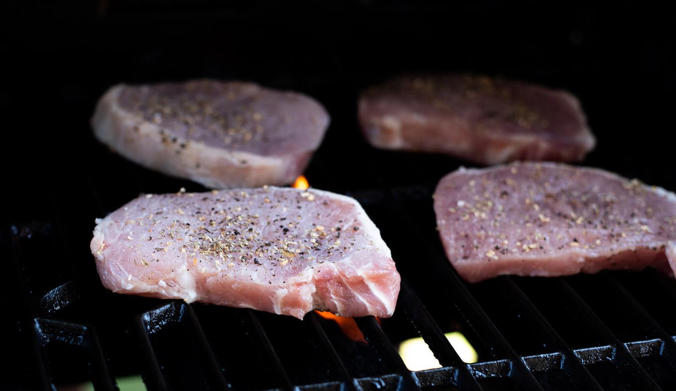 Seasoned pork chops cooking a gas grill.