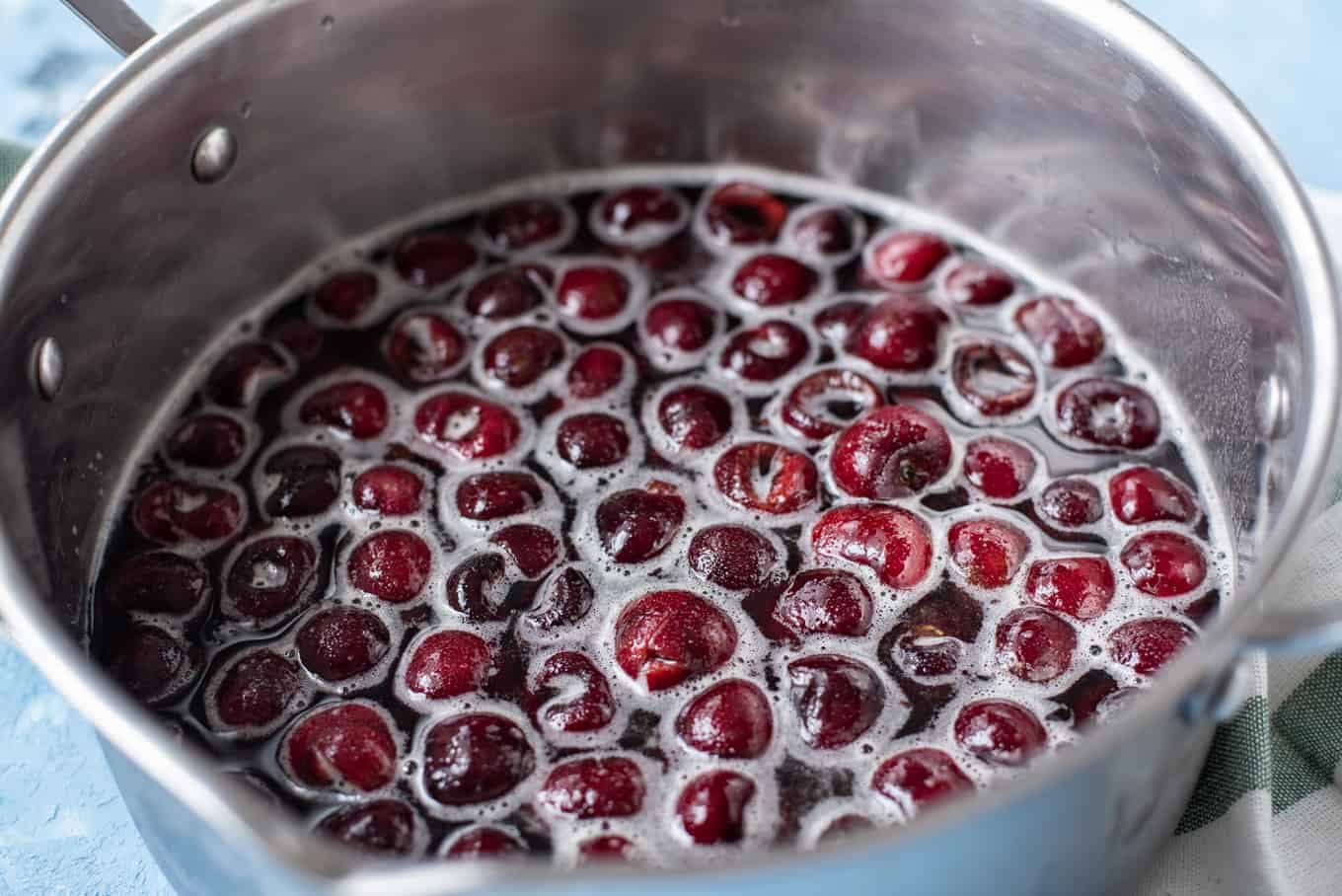 A saucepan of cherries with sugary liquid.