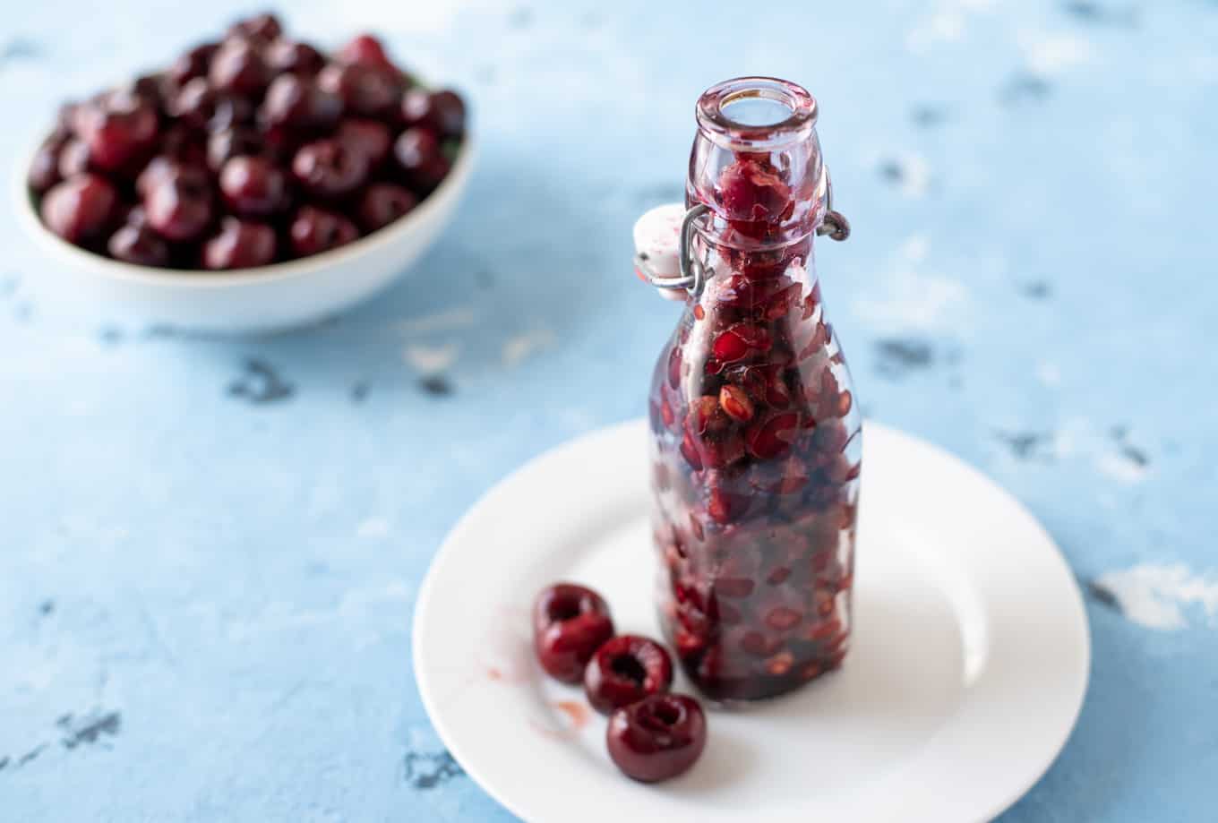 A bottle of cherry pits with some pitted cherries on a plate.