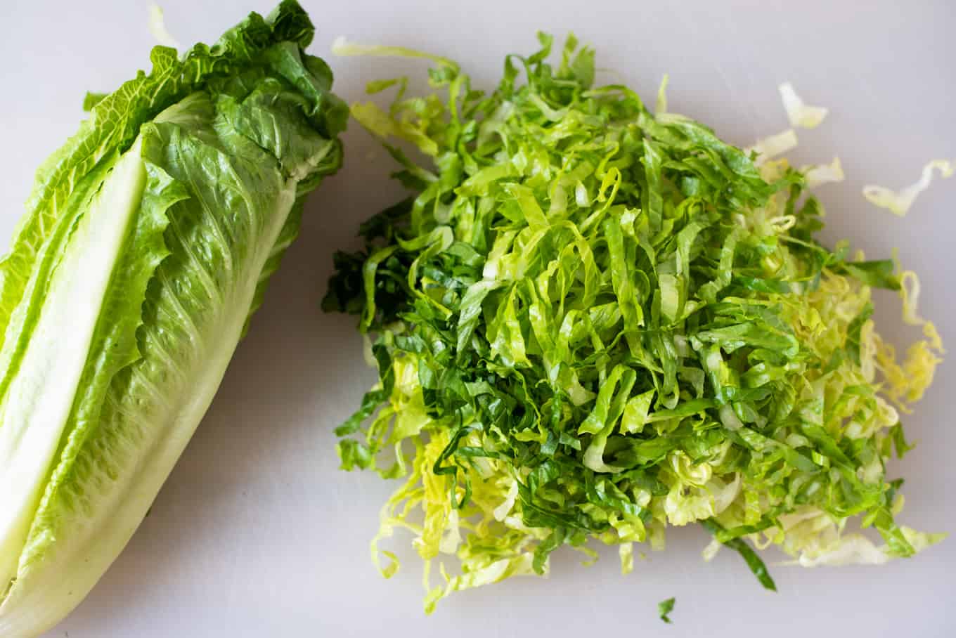 A head of romaine lettuce and thinly-sliced romaine lettuce on a cutting board.