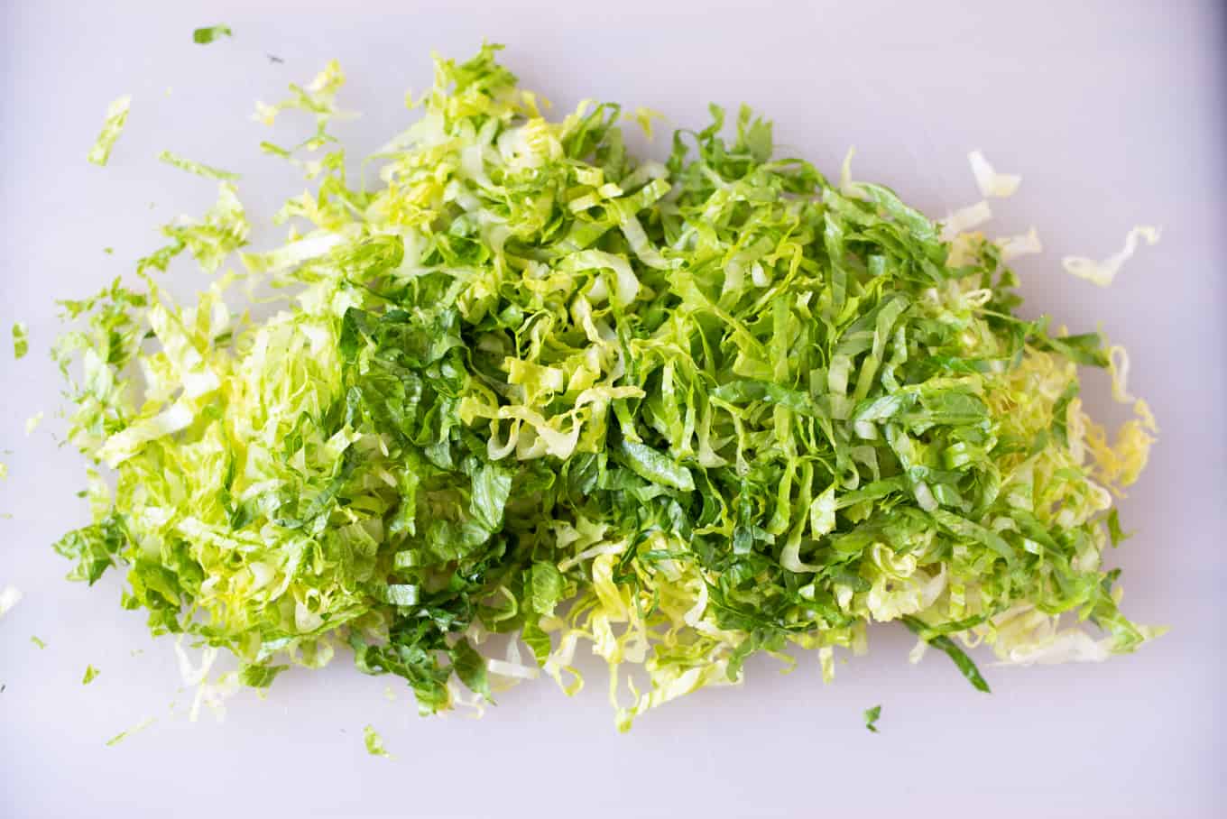 Thinly-sliced romaine lettuce on a cutting board.