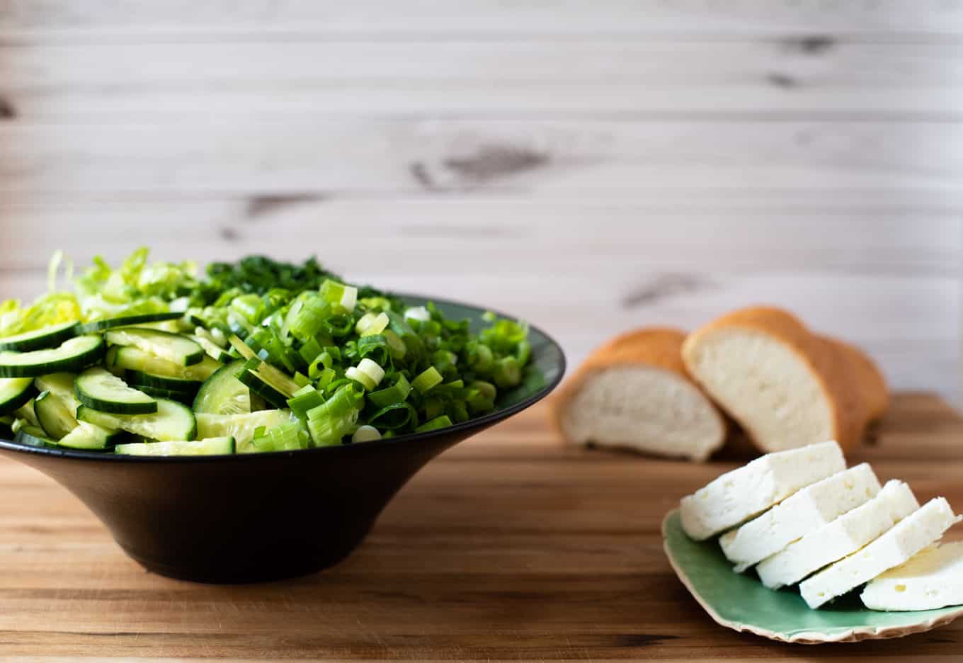 A close up of a Greek lettuce salad and feta cheese with bread in the background.