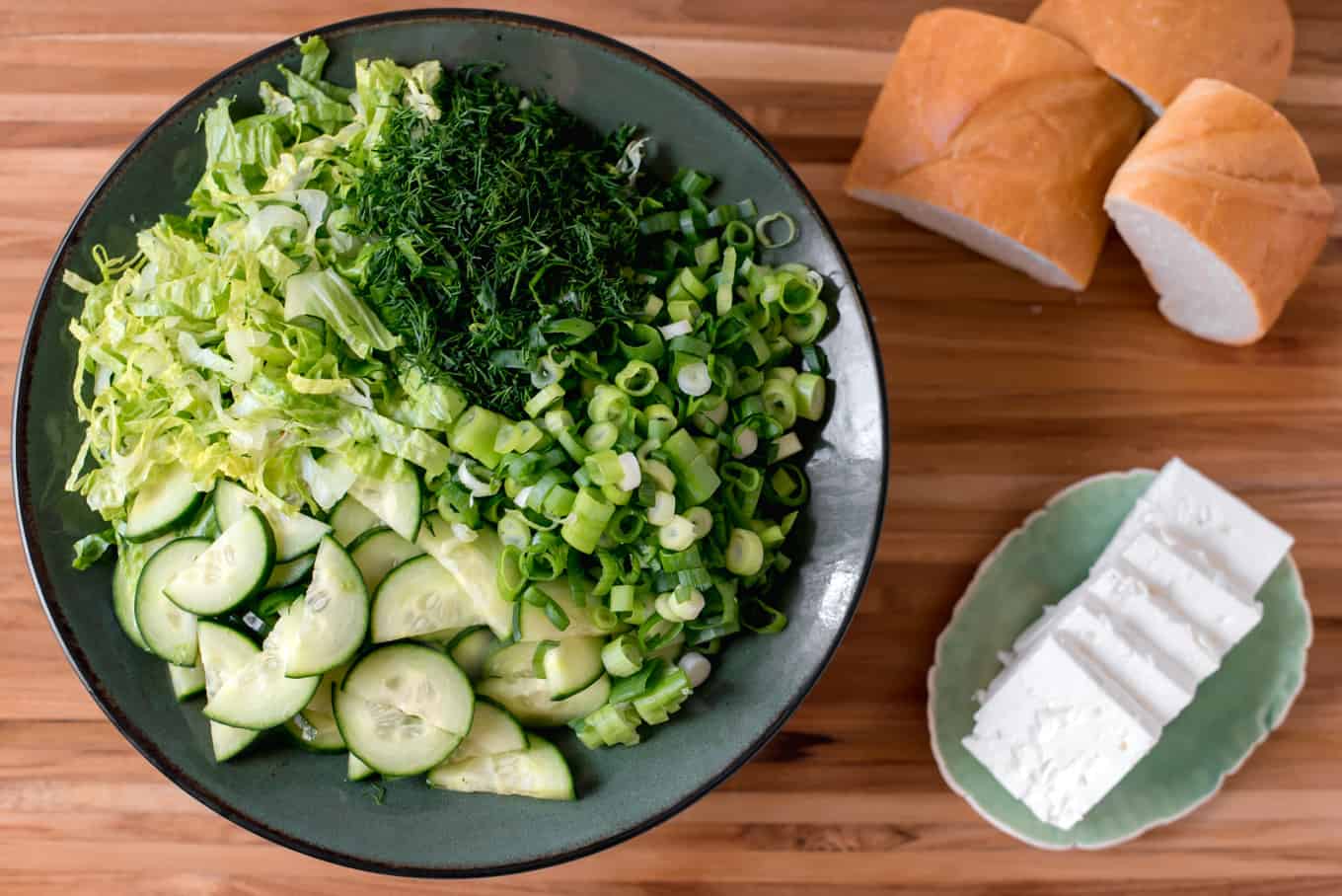 A bowl of Greek lettuce salad with bread and feta cheese on the side.