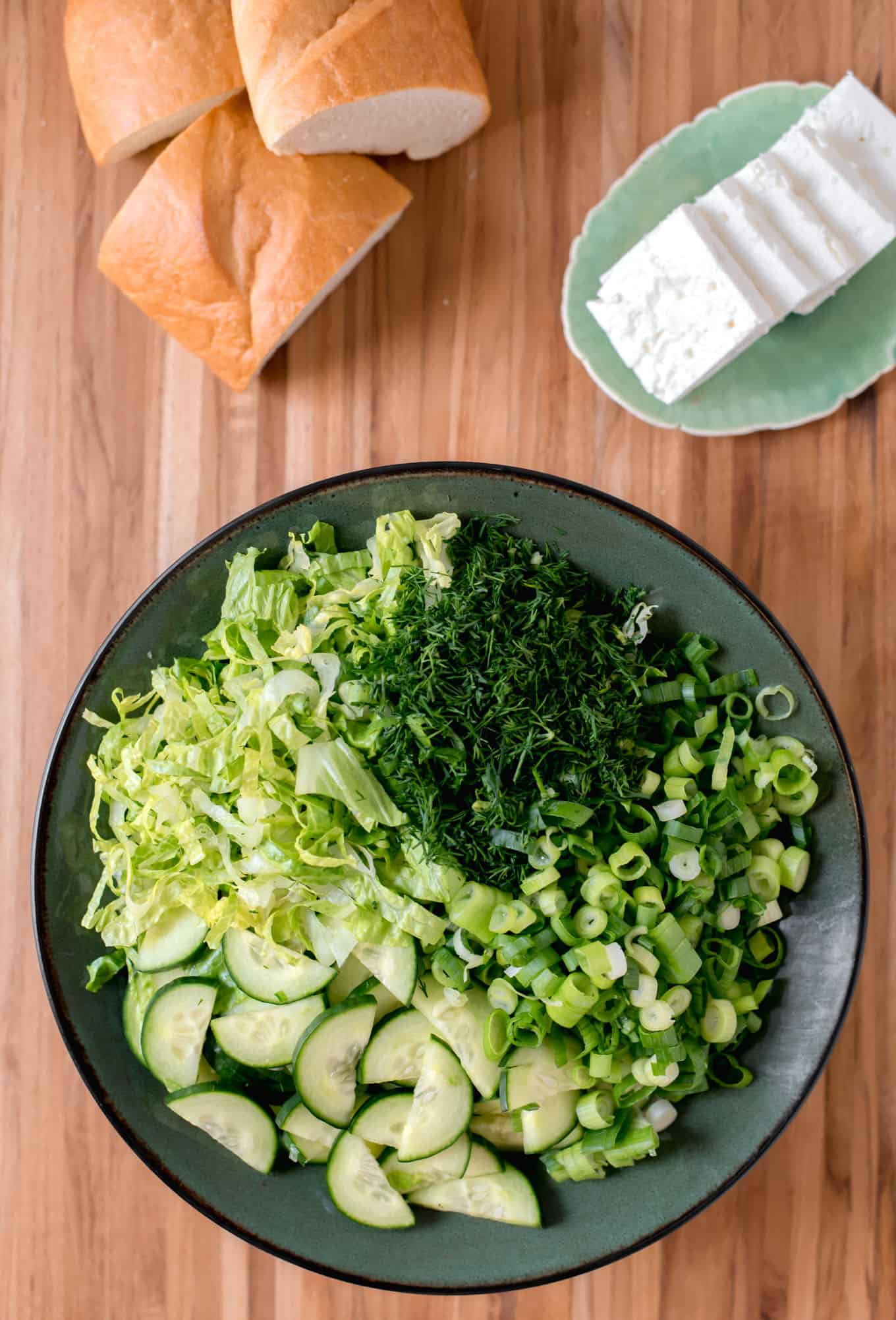 A bowl of Greek lettuce salad with bread and feta cheese on the side.