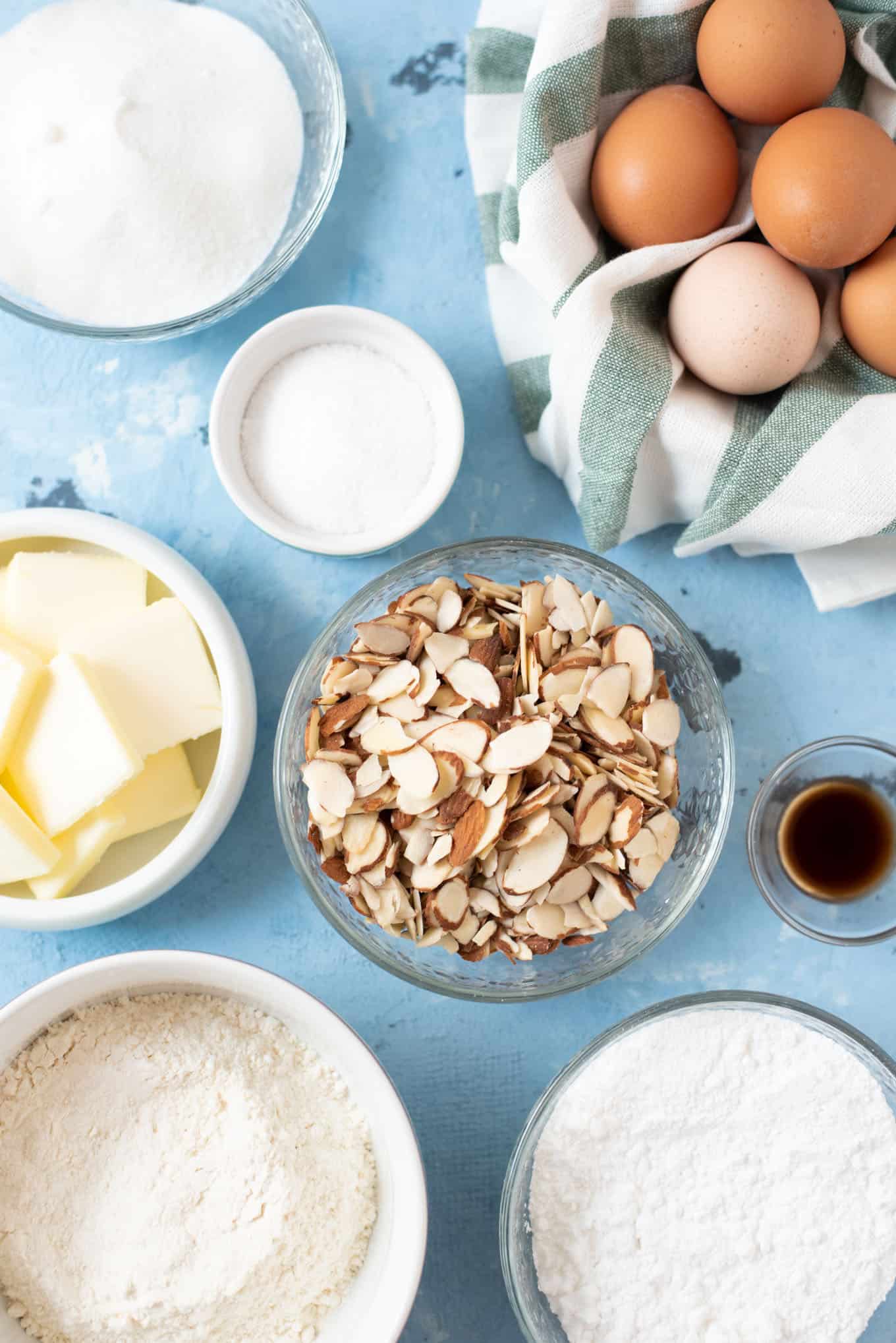 Bowls of butter, sliced almonds, sugar, flour, eggs, and vanilla extract.