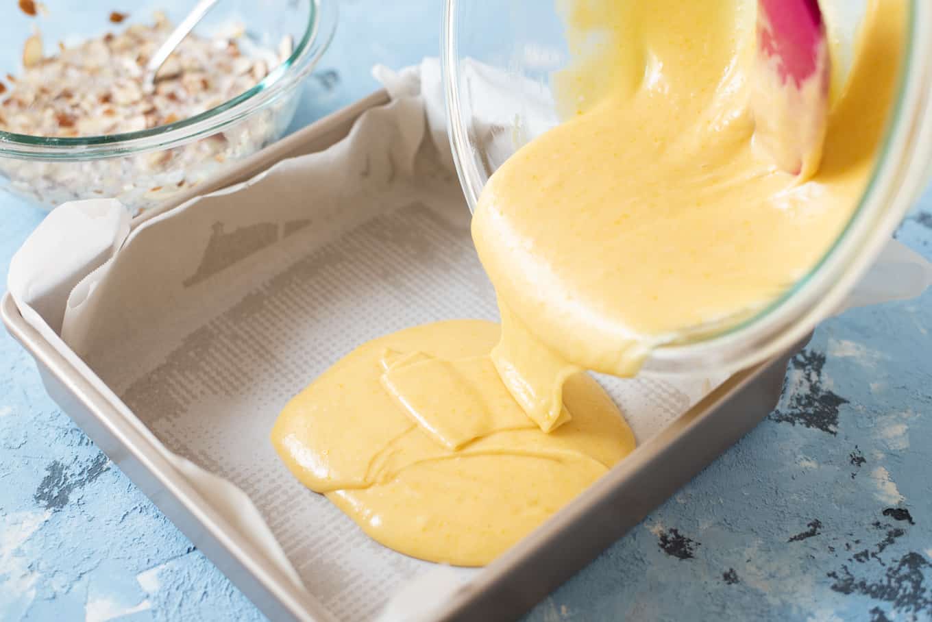 Batter being poured into a parchment-lined baking pan.