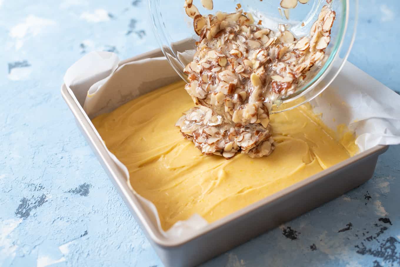 A baking pan of cake bar batter with almond-meringue mixture being poured on top.