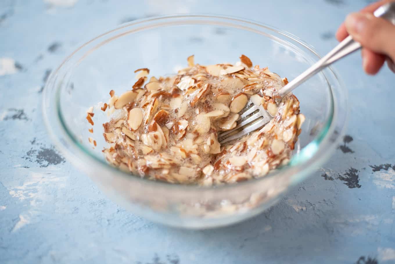 A mixture of sliced almonds, sugar, and egg whites in a small glass bowl.
