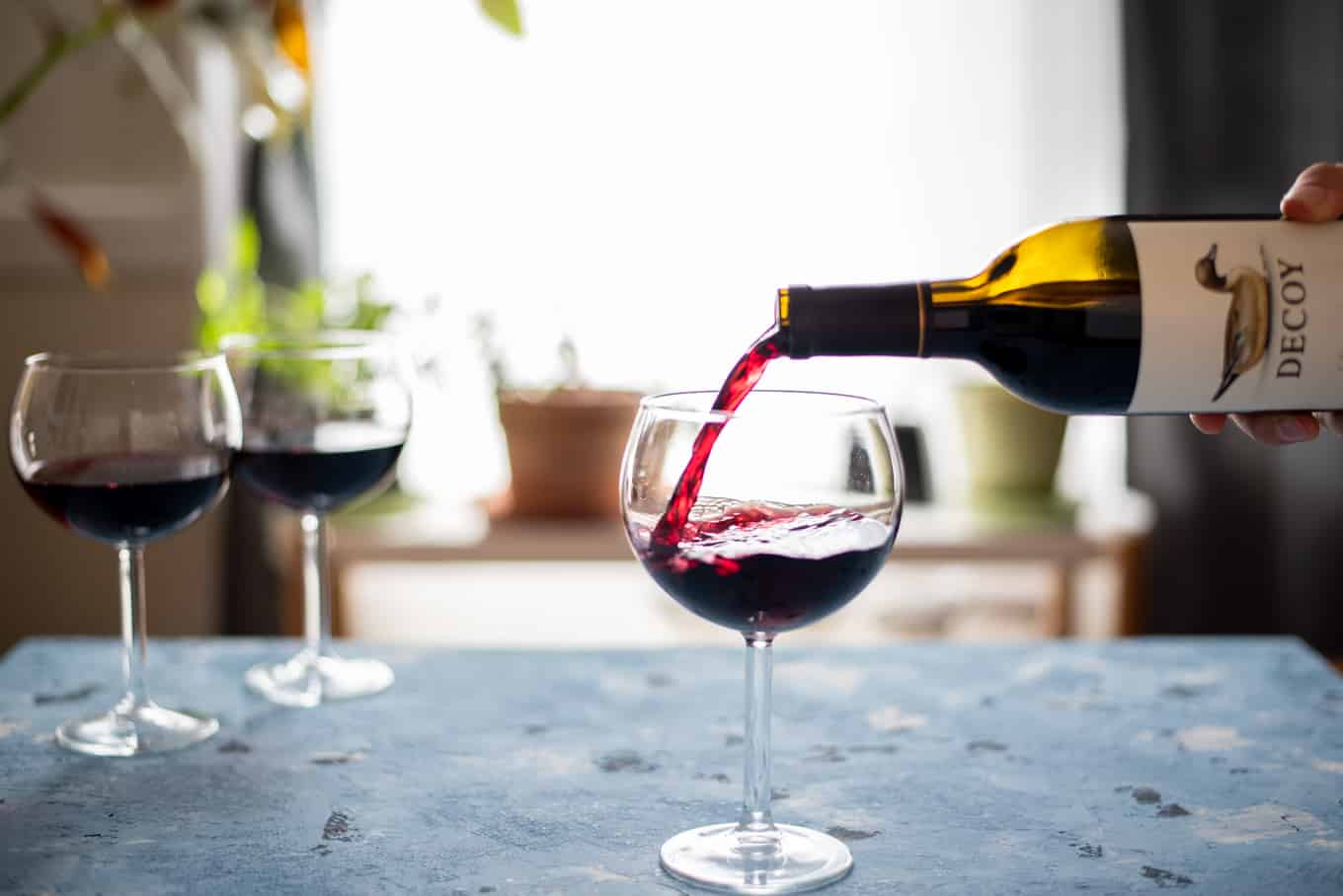 Red wine being poured into a stemmed wine glass.