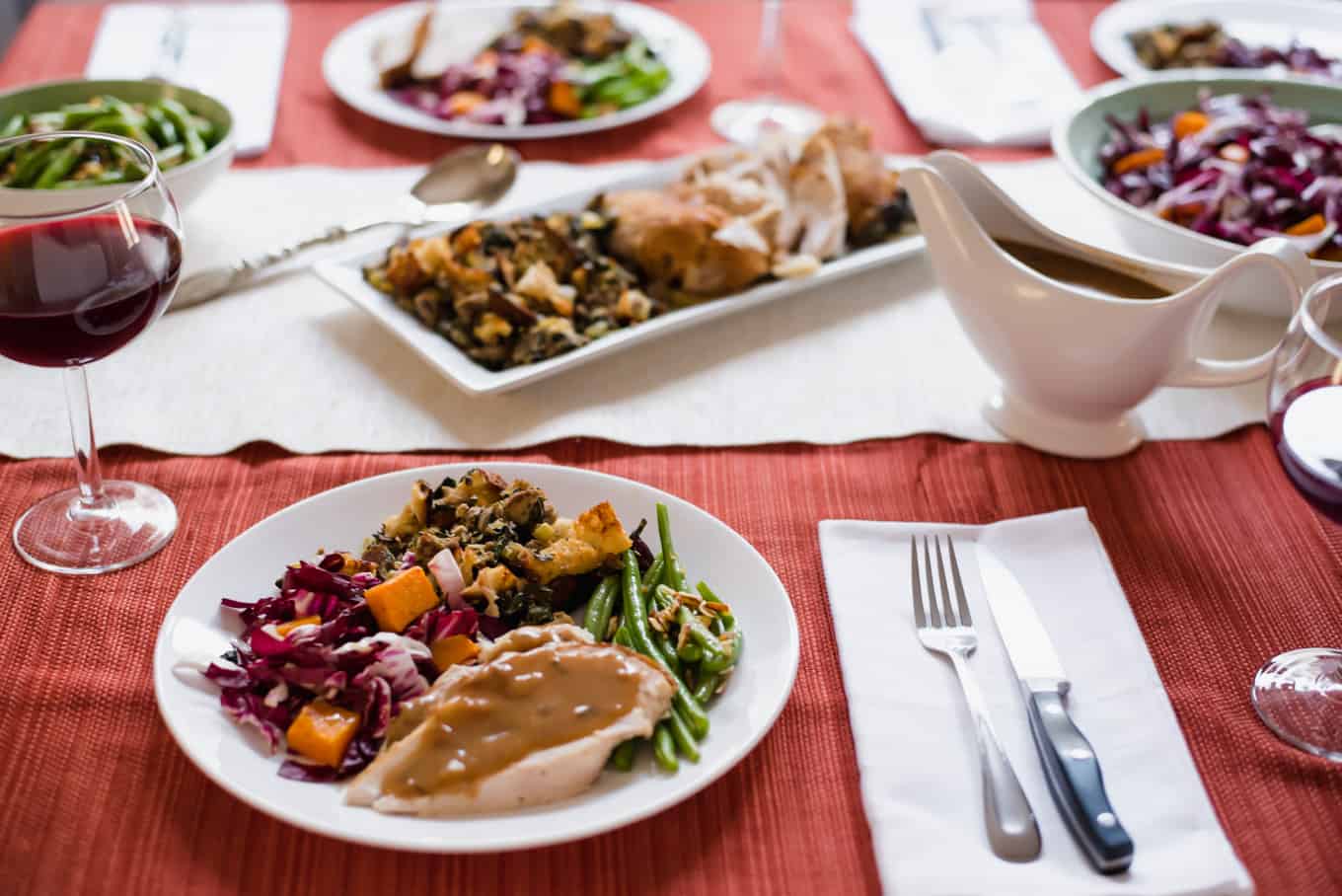 A table topped with plates of Thanksgiving dinner, utensils, and a gravy boat.