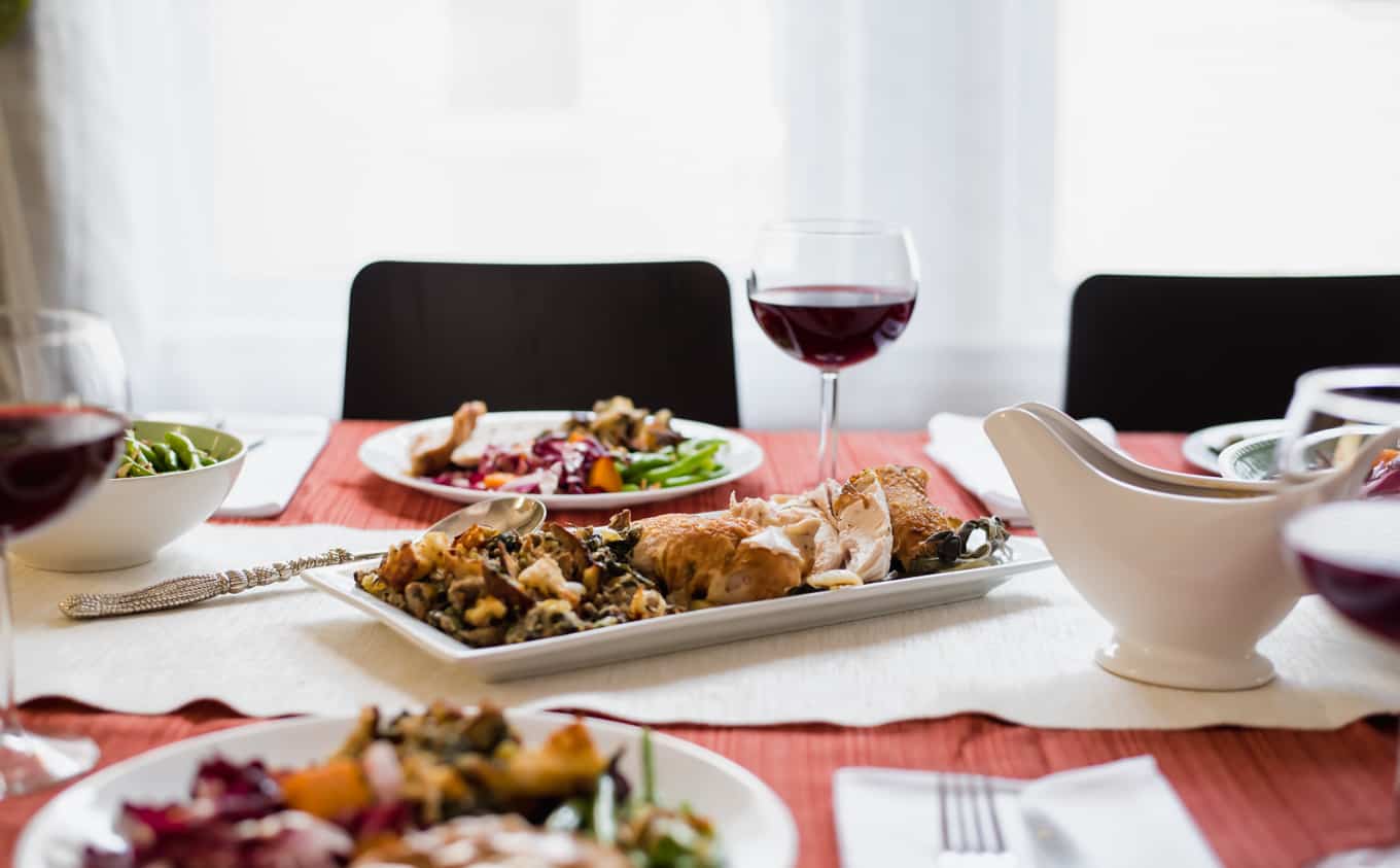 A small rectangular platter of roasted turkey and stuffing with a plate of food and red wine in the background.