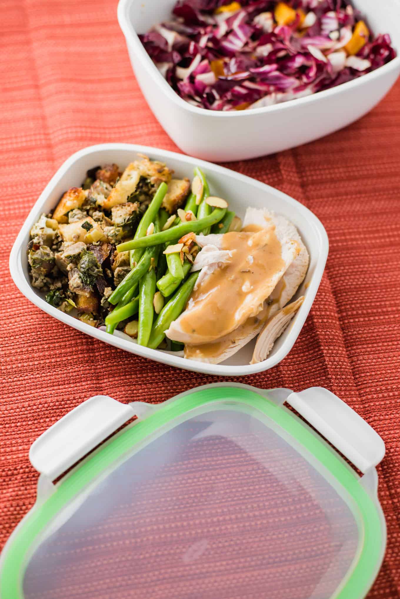 Roasted turkey topped with gravy in a food storage container with green beans and stuffing.