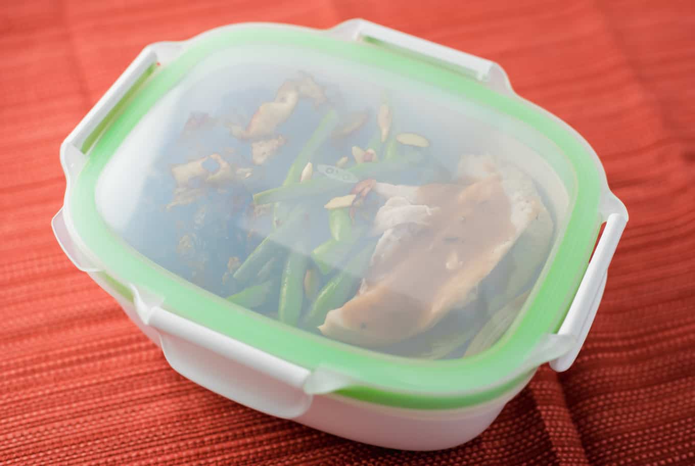 A plastic food storage container filled with food. Topped with a green lid.