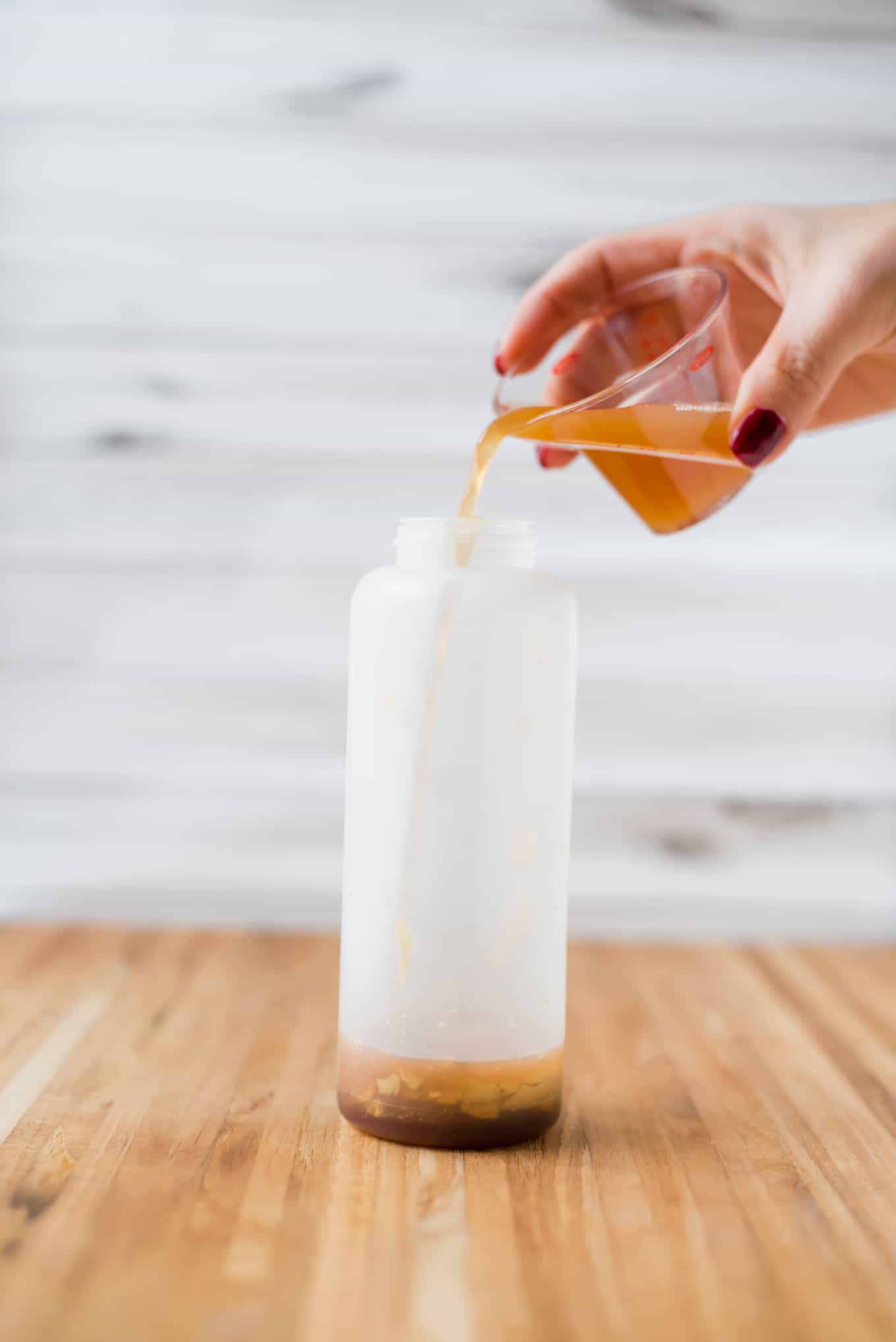A hand pouring vinegar into a plastic bottle.